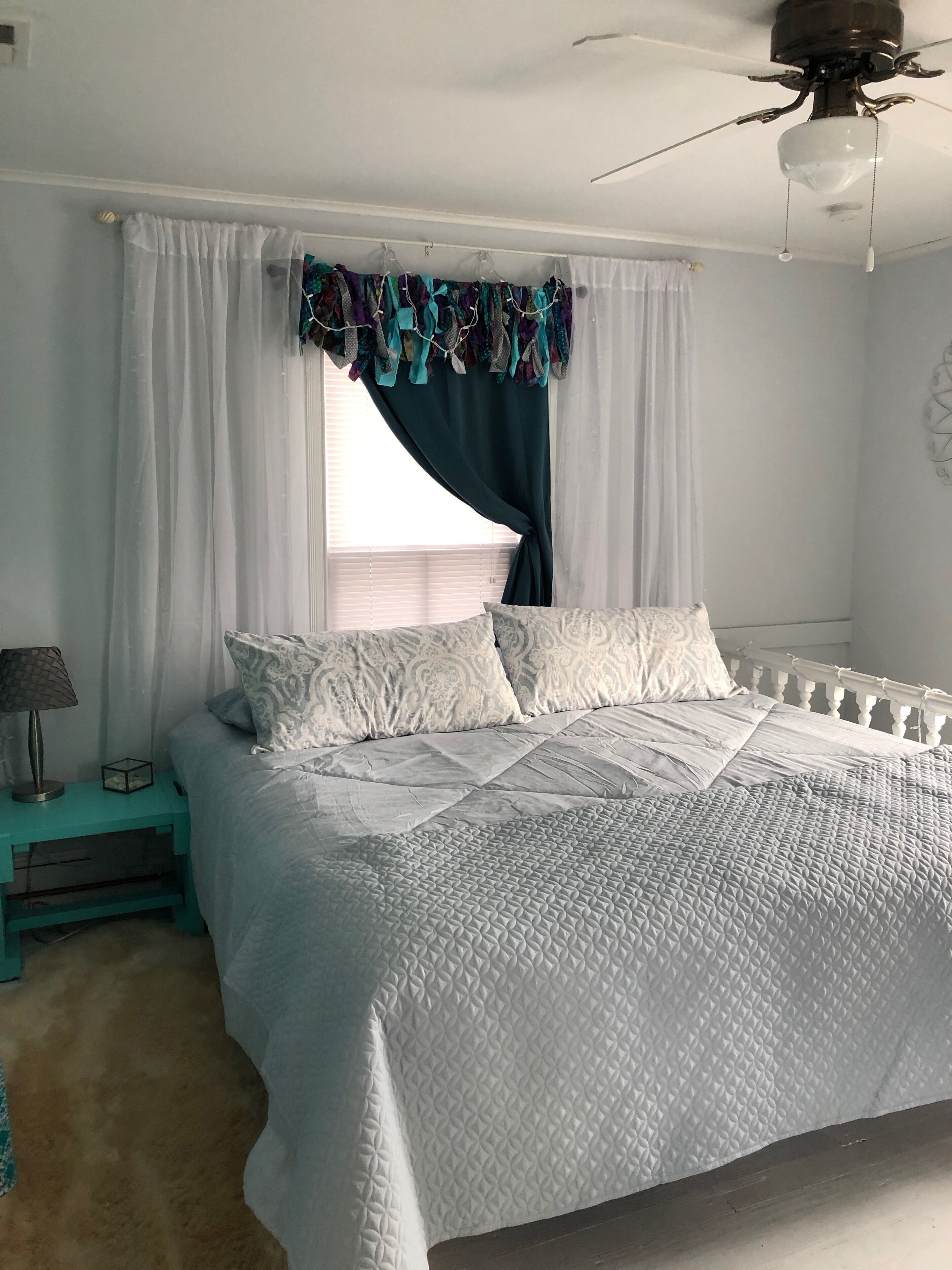 A bedroom with a bed, a nightstand, a ceiling fan, and a window with curtains.