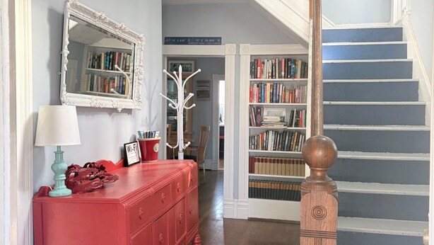 Eine Treppe mit einem hölzernen Geländer und einem weißen Handlauf, die zu einem Raum führt, in dem ein roter Kommode, eine weiße Lampe und ein Spiegel zu sehen sind.