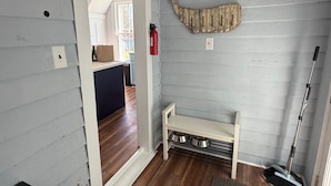 Ein Zimmer mit einer hölzernen Sitzbank, einem Feuerlöscher, einer Futterstelle für Haustiere und einem Spiegel an der Wand.