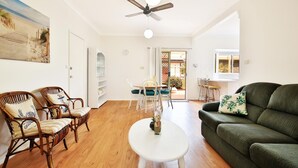 Ein Wohnzimmer mit Holzboden, einem grünen Sofa, Korbst ühlen, einem weißen Couchtisch und einem Deckenventilator.