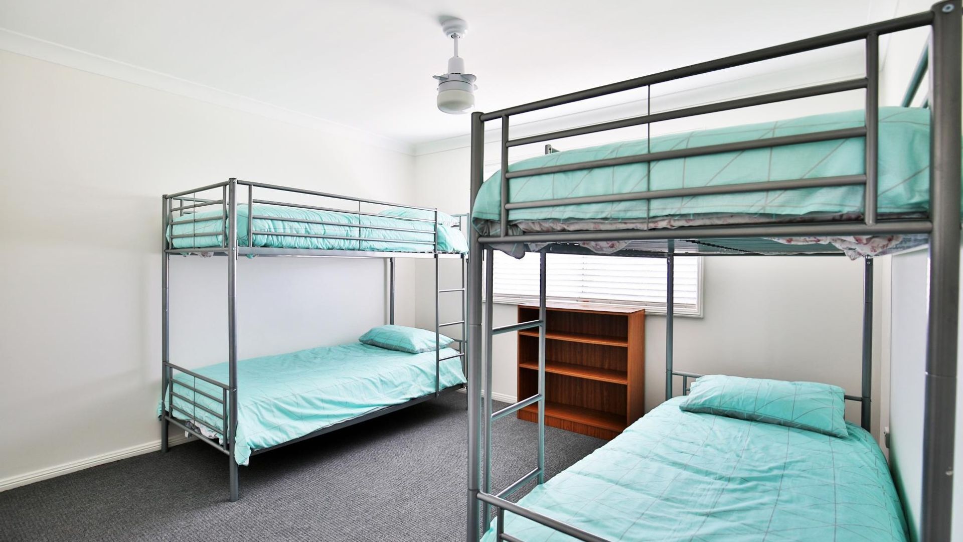 A dormitory room with bunk beds, a ceiling fan, and a window with blinds.