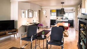 A modern living room with a flat-screen TV, two black chairs, a small table with a potted plant, and a dining area with a wooden table and red chairs. - Updated Tacoma Home w/ Patio: 3 Mi to Downtown (Tacoma)