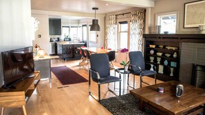 A modern living room with a TV, wooden coffee table, and comfortable seating. A kitchen with a dining area is visible in the background. - Updated Tacoma Home w/ Patio: 3 Mi to Downtown (Tacoma)