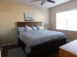 A bedroom with a bed, a ceiling fan, a window, and a painting on the wall.