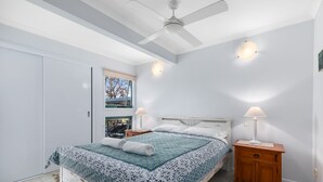 Un dormitorio con cama, mesitas de noche, ventilador de techo y ventana con vistas.