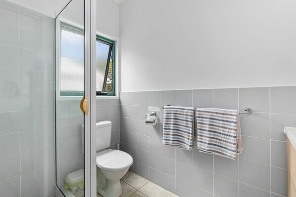 Un baño con inodoro, zona de ducha y toallero con dos toallas.