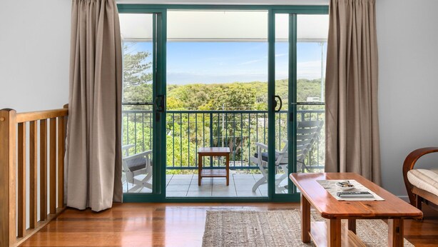 Una habitación con puerta corrediza de vidrio que da a un balcón con vistas a la vegetación y un cielo despejado.