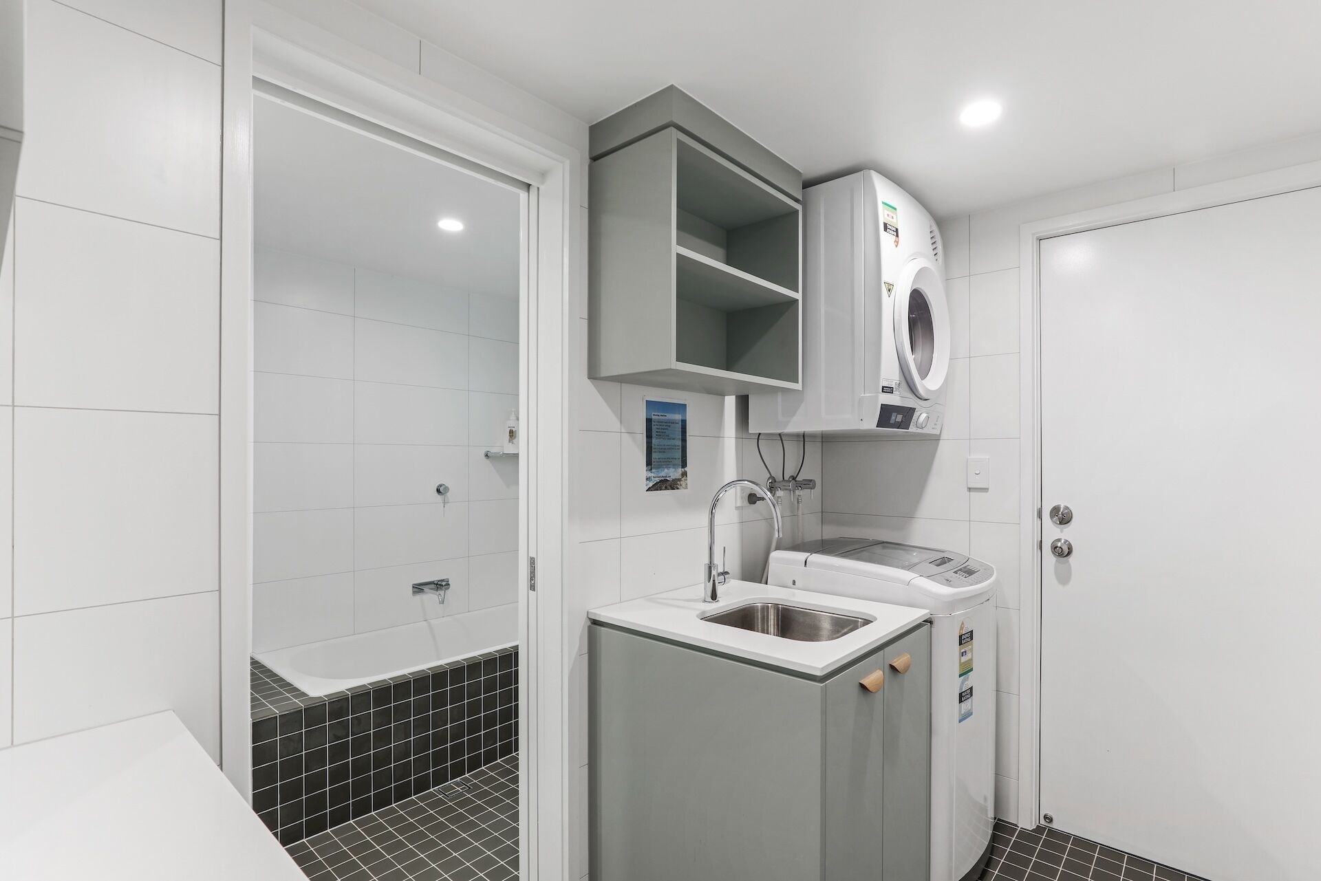 Une salle de bain moderne équipée d’un lave-linge intégré, d’un lavabo et d’un espace douche.