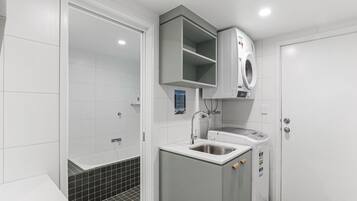 Une salle de bain moderne équipée d’un lave-linge intégré, d’un lavabo et d’un espace douche.