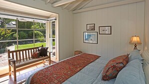 A bedroom with a large bed, a bench, and a window overlooking a garden. - Rincon Retreat - Casual Beachfront Comfort (Carpinteria)