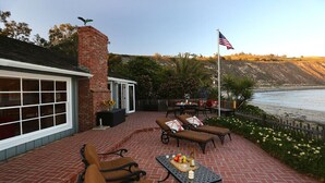A patio with outdoor furniture, a table with drinks, and a view of the ocean. - Rincon Retreat - Casual Beachfront Comfort (Carpinteria)