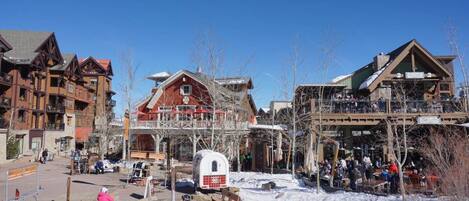 A snow-covered outdoor area with wooden buildings, a covered seating area, and a white RV parked nearby.