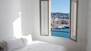 A hotel room with a large window offering a view of a marina and buildings. - Waterfront panoramic sea view with balcony, AC (Nice)