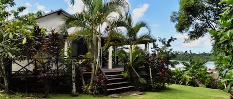 A house with a wooden deck, surrounded by lush greenery and a clear view of the sea.