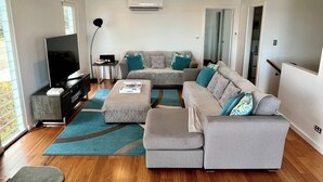 Un salon moderne avec un canapé gris, un téléviseur à écran plat, une table d’appoint et un tapis bleu.