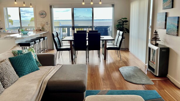 Un salon moderne avec un coin repas, de grandes fenêtres et une vue sur la mer.