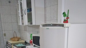 Een kleine keuken met witte kastjes, een witte koelkast, een magnetron en een fornuis.