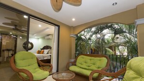A balcony with wicker furniture and a view of palm trees. - Tropical Oasis Retreat: Luxe Condo Steps from Jaco Beach & Amenities (Jaco)