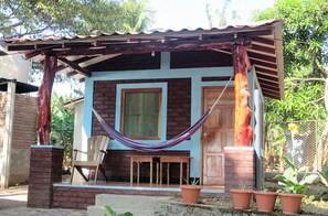 Une maison à deux étages, avec un toit en tuiles, un porche à l’avant et un hamac.