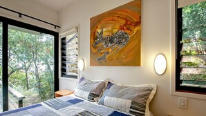 Un dormitorio con una cama grande, vistas a árboles por la ventana y un cuadro en la pared.