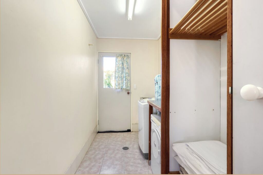 Une petite salle de bain comprenant un lave-linge, un petit lavabo et une étagère en bois.
