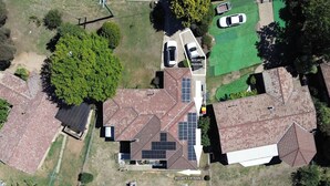Ein Luftbild eines Wohngebiets mit einem Haus, das ein Solardach, eine Auffahrt und einen Parkplatz mit der Aufschrift 'BeeJay's Parking' zeigt.