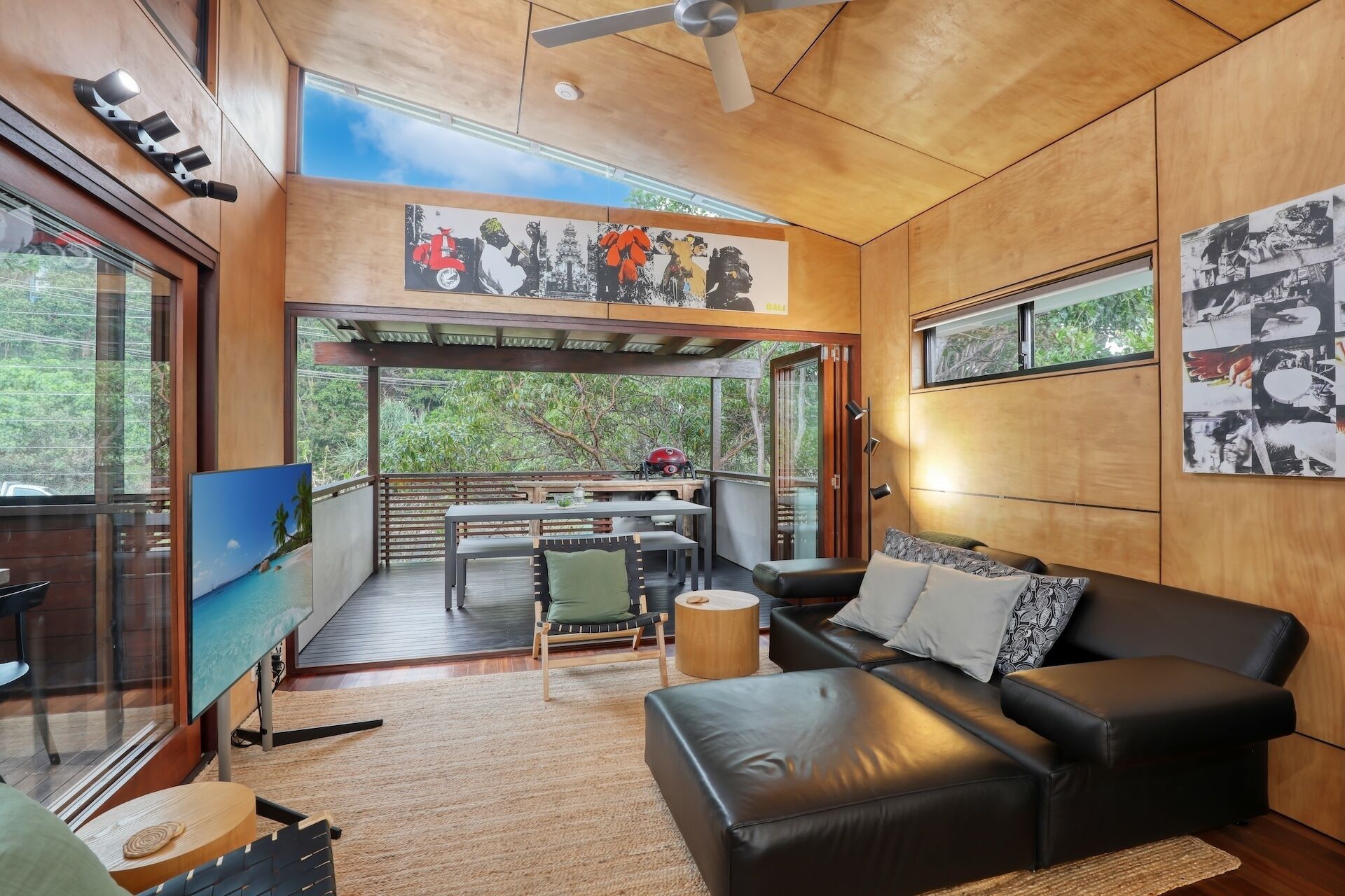 A modern living room with a black leather sofa, a wooden dining table, and a TV.