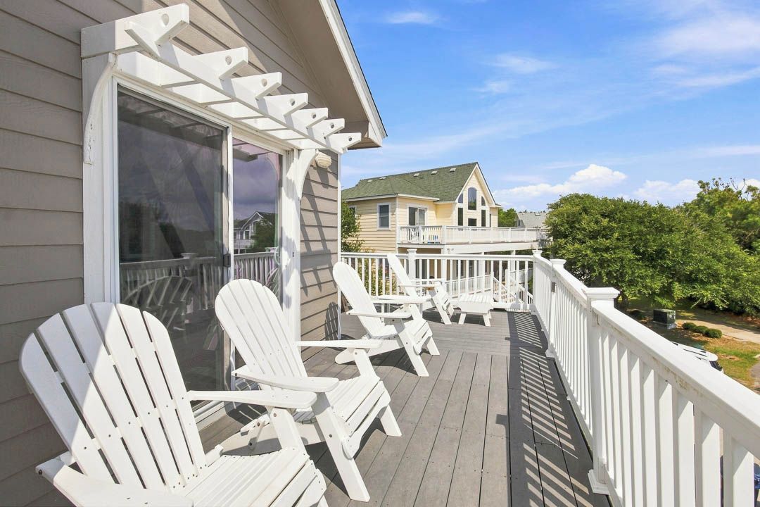 A wooden deck with white railings and several Adirondack chairs.