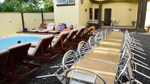 A poolside area with lounge chairs and a table, a covered seating area, and a building with a door and windows. - Residence Orchid (Mont Choisy)