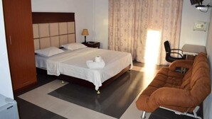 A hotel room with a double bed, a bedside table with a lamp, a brown armchair, and a wardrobe. - Residence Orchid (Mont Choisy)