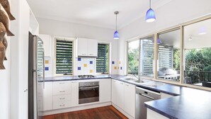A modern kitchen with white cabinets, a built-in oven, a dishwasher, and a large window with a view of greenery. - Spacious home with views suitable for 2 families (Point Lookout)