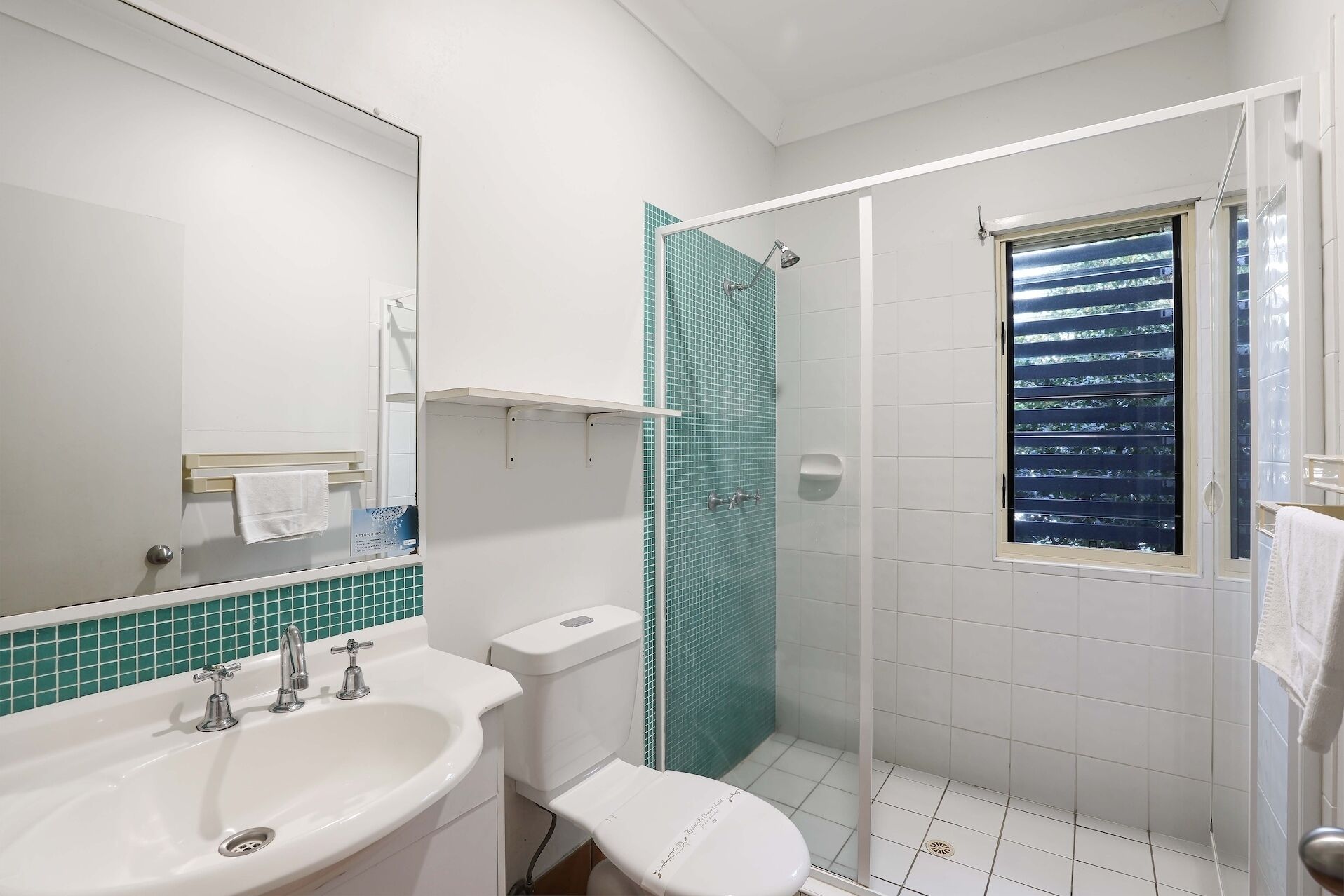 A bathroom with a white sink, a toilet, a shower with a glass door, and a window with a view of the sky.