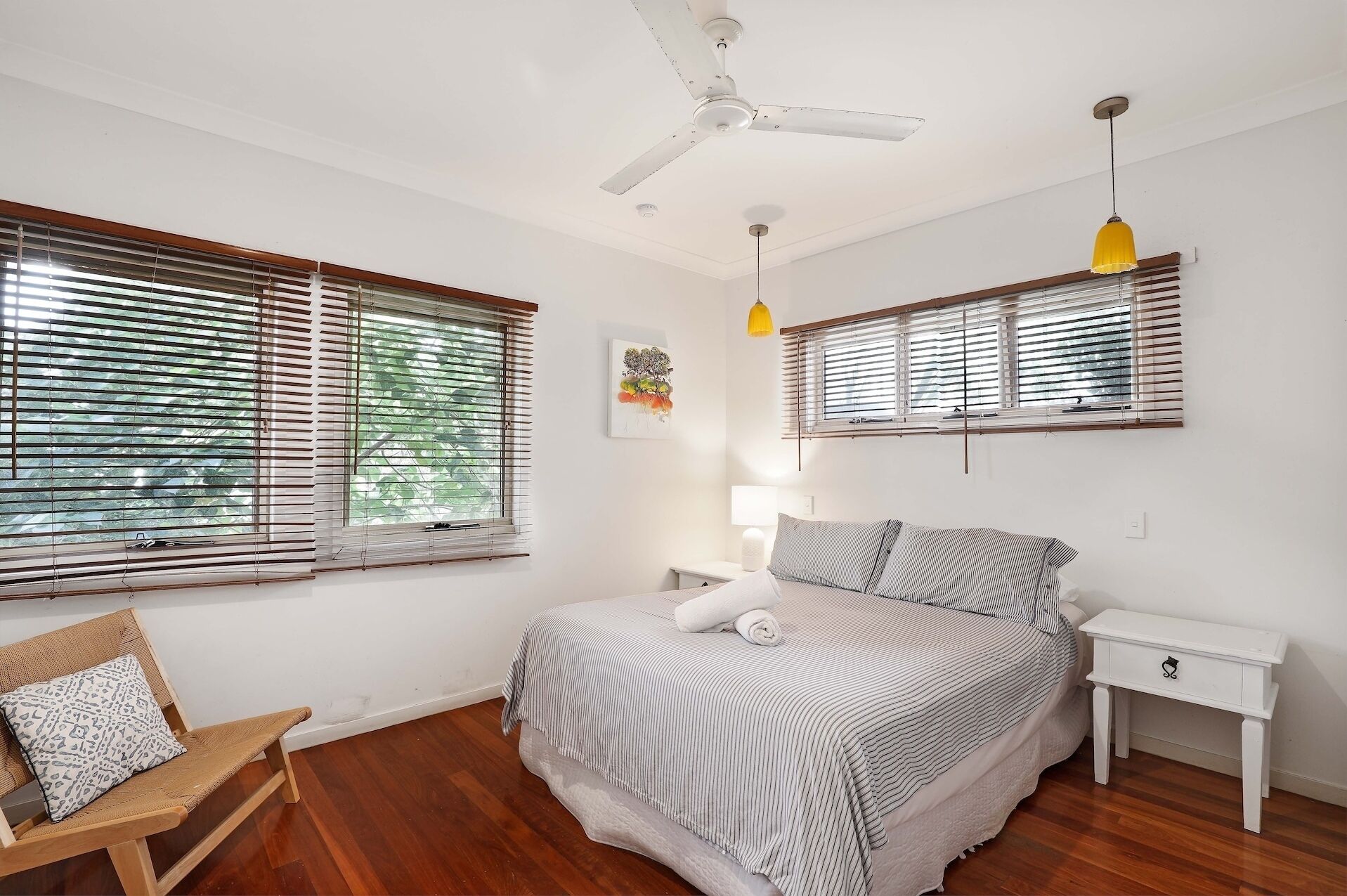 Une chambre à coucher comprenant un lit, deux tables de chevet, une chaise et un ventilateur de plafond.