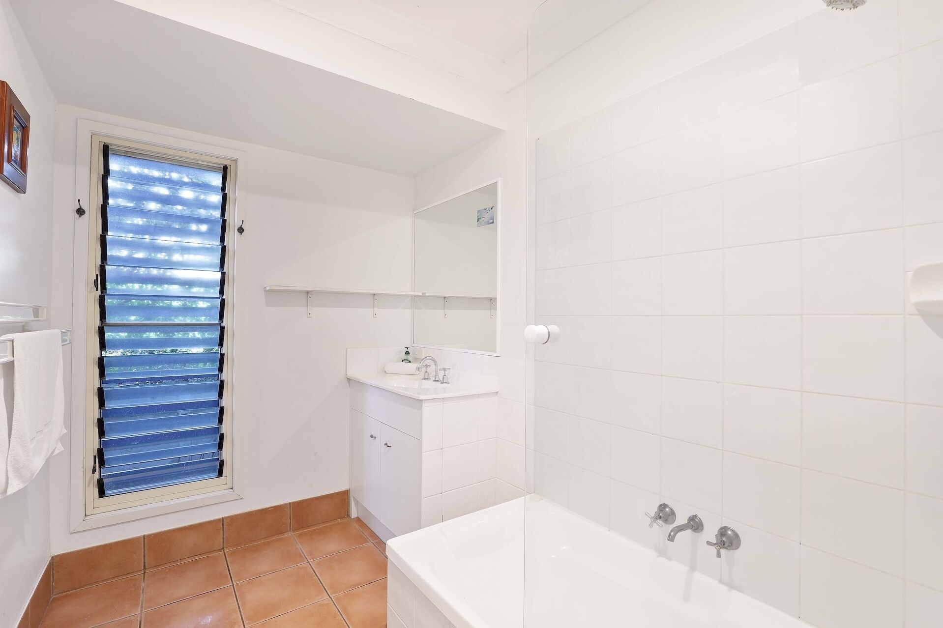 A bathroom with a bathtub, a sink, and a window with blinds.