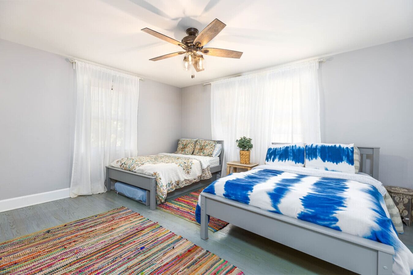Une chambre avec deux lits, un ventilateur de plafond et un tapis rayé aux couleurs vives.