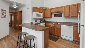 Une cuisine moderne avec des meubles en bois, un four à micro-ondes, une cuisinière et un lave-vaisselle. Il y a deux tabourets près de l’îlot central.