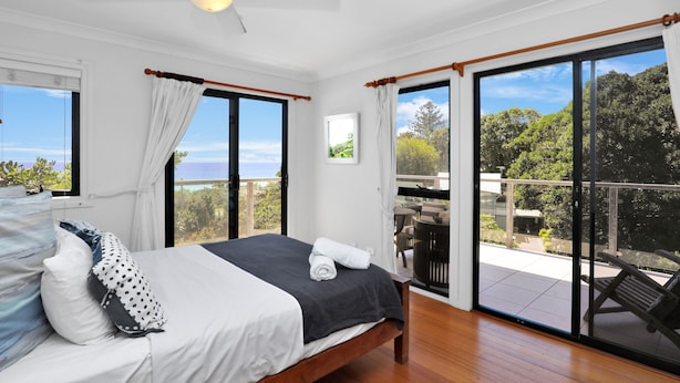 Un dormitorio con cama, ventilador de techo y vistas a un balcón con mobiliario exterior.
