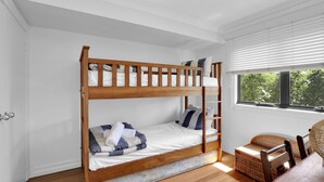 Una cama litera con estructura de madera, ropa de cama blanca y una pequeña silla de mimbre al lado.