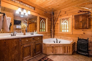 Une salle de bain de style rustique, avec des murs en bois, un grand meuble-lavabo, une baignoire sur pieds et un miroir avec des lumières au-dessus.
