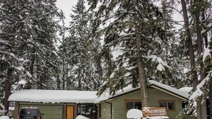 Una cabaña rústica con un letrero que dice "Auberge Kicking Horse" rodeada de árboles cubiertos de nieve.