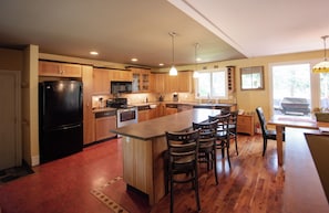 Una cocina amplia con armarios de madera, una isla central con taburetes de bar, un refrigerador, un microondas y una estufa.