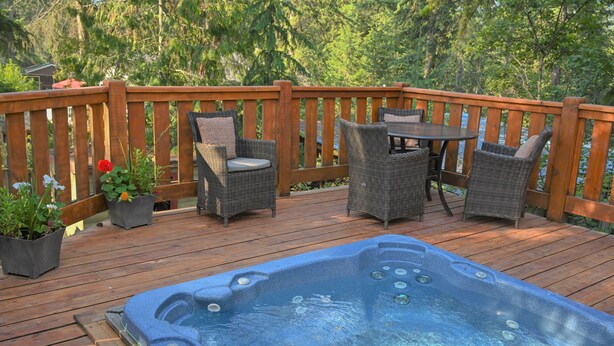 Una terraza de madera con un jacuzzi, sillas de mimbre y una mesa.