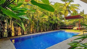 Ein Schwimmbecken, umgeben von üppiger tropischer Vegetation, darunter Bananenstauden und Palmen.