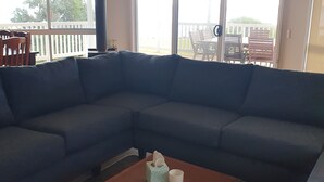 A living room with a large L-shaped sectional sofa, a wooden coffee table with a tissue box and a candle, and a view of a balcony with outdoor furniture. - Bella Views -  Beach front, WiFi and Foxtel!
Availability School Holidays (Ventnor)