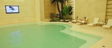 An indoor swimming pool with lounge chairs and palm plants.