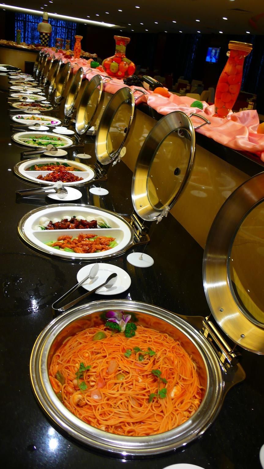 A buffet line with various dishes and a large pot of noodles.