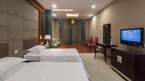Habitación de hotel con tres camas, un escritorio con televisor, un espejo y una silla.