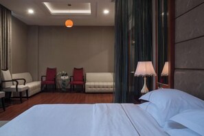 A hotel room with a large bed, two armchairs, a small table with a vase, and a lamp. - Osotto Recreation Hotel (Foshan)