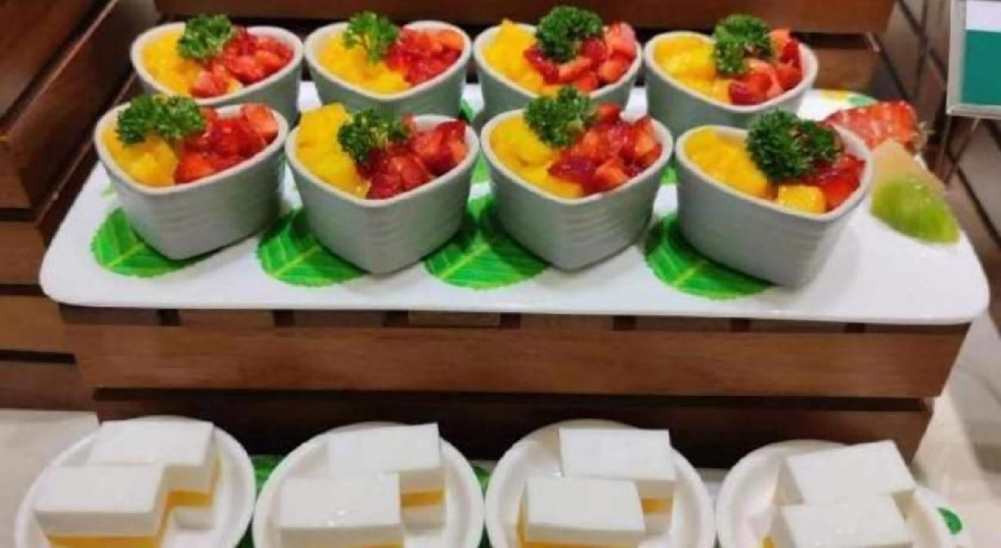 Een presentatie van etenswaren, waaronder schalen met fruit en bladeren, en rechthoekige lekkernijen op een dienblad.