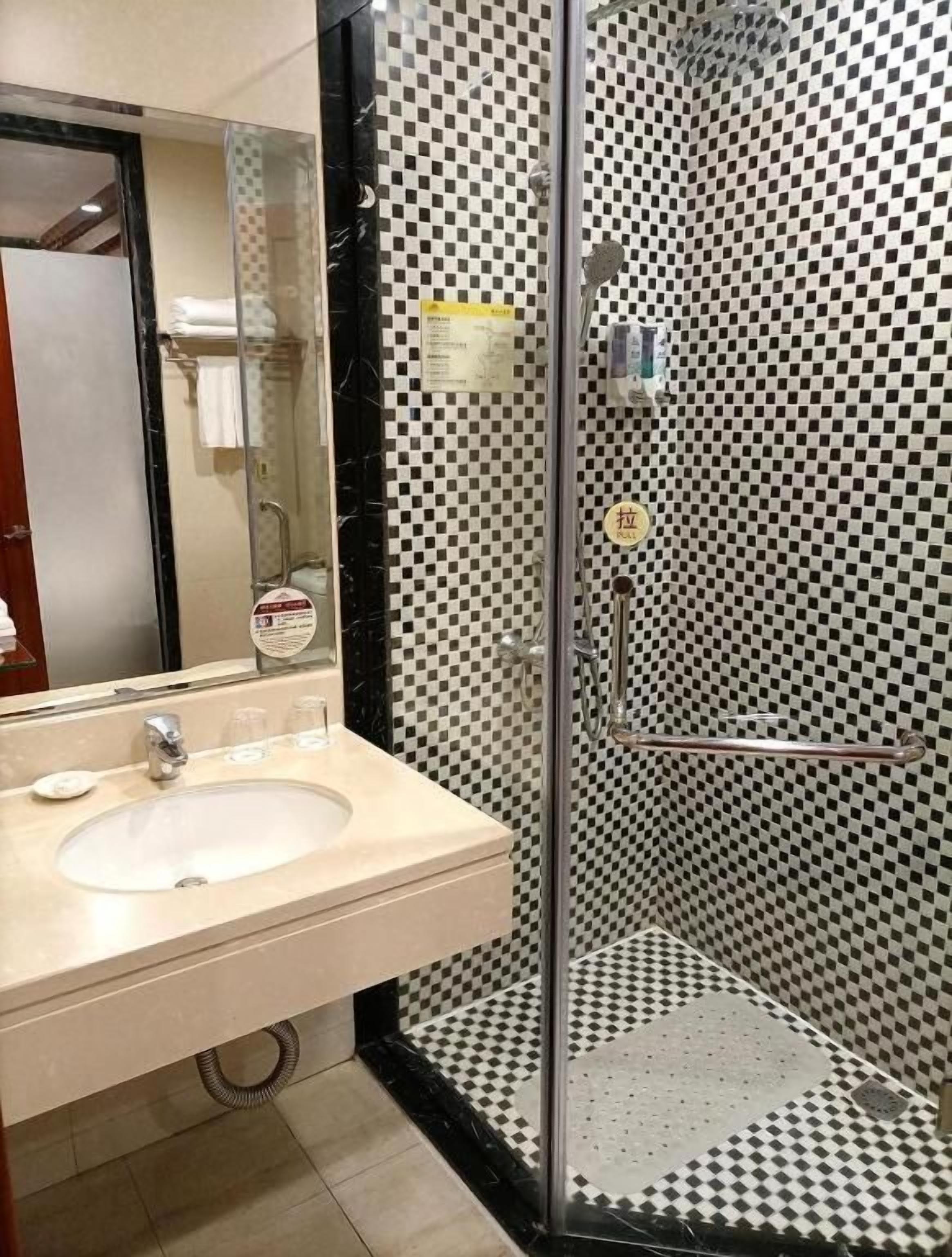 A bathroom with a checkered floor, a sink with a mirror, and a glass-enclosed shower area.